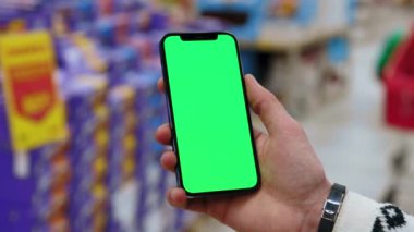 Yavaş çekimde çalışan adam arka planda bulanık, dikey yeşil ekranlı cep telefonu kullanır. Kapalı alanda dokunmatik ekranlı müşteri boş cep telefonu. Kapat.