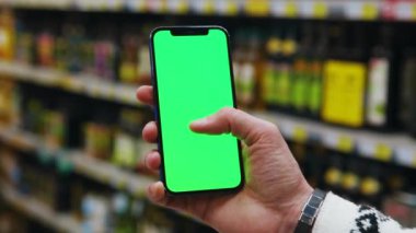 Kapat ellerini adamım. Arka planda bulanık süpermarkette dikey yeşil ekranlı cep telefonu kullan. Kapalı alanda dokunmatik ekranlı müşteri boş cep telefonu. Yavaş çekim