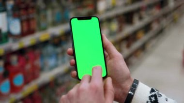 Genç eller, arka planda bulanık süpermarkette dikey yeşil ekranlı cep telefonu kullanır. Kapalı alanda dokunmatik ekranlı müşteri boş cep telefonu. Yavaş çekim