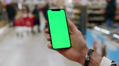 Kapalı eller, arka planda bulanık insanlar yürürken arka planda dikey yeşil ekranlı akıllı telefon kullanır. Model dinleme görüntülü kromakey telefon. Yavaş çekim