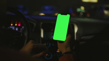 Kapalı el adam geceleri arabada dikey yeşil ekranlı akıllı telefon kullanır. Cihaz dijital cihaz, dokunmatik ekranlı mobil telefon teknolojisi. Yavaş çekim