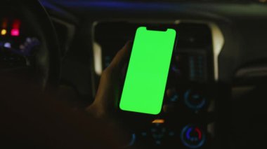 Eller geceleri arabada dikey yeşil ekranlı akıllı telefon kullanır. Cihaz dijital cihaz, dokunmatik ekranlı mobil telefon teknolojisi. Yavaş çekim