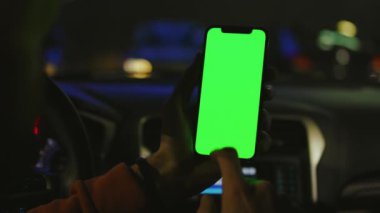 Eller geceleri arabada dikey yeşil ekranlı akıllı telefon kullanır. Cihaz dijital cihaz, dokunmatik ekranlı mobil telefon teknolojisi. Yavaş çekim
