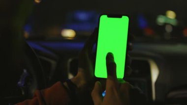 Arabadaki adam geceleri dikey yeşil ekranlı akıllı telefonu kullanır. Cihaz dijital cihaz, dokunmatik ekranlı mobil telefon teknolojisi. Yavaş çekim