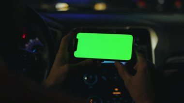 Kapatın ellerinizi, geceleri arabanızda yatay yeşil ekranlı akıllı telefon kullanın. Cihaz dijital cihaz, dokunmatik ekranlı mobil telefon teknolojisi. Yavaş çekim