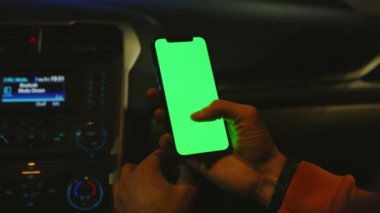 Adam geceleri arabasında dikey yeşil ekranlı telefonu tutuyor. Cihaz dijital cihaz, dokunmatik ekranlı mobil telefon teknolojisi. Kapatın. Yavaş çekim