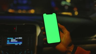 Arabada geceleri dikey yeşil ekranlı cep telefonu kullanılıyor. Cihaz dijital cihaz, dokunmatik ekranlı mobil telefon teknolojisi. Kapatın. Yavaş çekim