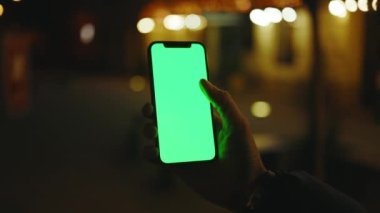 Gece Sokağında dikey yeşil ekran standı olan bir telefon kullan. İyi akşamlar akıllı telefon ekran uygulaması. Teknoloji dokunmatik hücre ekranı. Yavaş çekim