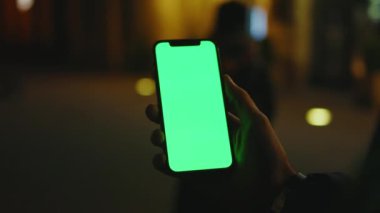 Geceleri genç adamlar şehir caddesinde dikey yeşil ekranlı telefon kullanırlar. İyi akşamlar akıllı telefon ekran uygulaması. Teknoloji dokunmatik hücre ekranı. Yavaş çekim