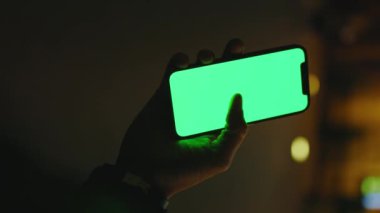 Dikey çekim yapan eller gece caddesinde dikey yeşil ekranlı telefon kullanıyor. İyi akşamlar akıllı telefon ekran uygulaması. Teknoloji dokunmatik hücre ekranı. Yavaş çekim