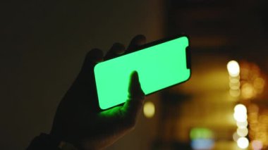 Eller yukarı. Gece caddesinde dikey yeşil ekran standı olan telefonu kullan. İyi akşamlar akıllı telefon ekran uygulaması. Dikey çekim. Teknoloji dokunmatik cep telefonu. Yavaş çekim