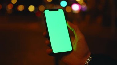 Kapatın elleri adamım. Gece şehir arka planında dikey yeşil ekranlı telefon kullanın. İyi akşamlar akıllı telefon ekran uygulaması. Teknoloji dokunmatik hücre ekranı. Yavaş çekim