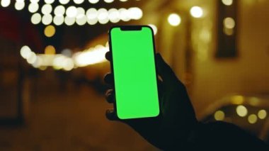 Arka plandaki çelenklerde dikey yeşil ekranlı cep telefonu tutan ağır çekimli bir adam. Mobil internet bağlantısı teknolojisi cihaz hücresi. Kapat.