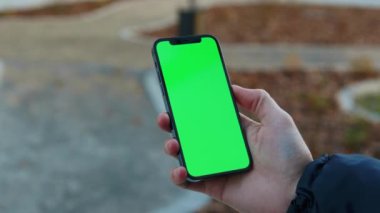 NEW YORK - 19 Aralık 2020: Şehrin arka planında dikey yeşil ekran güneş ışığı yolu ile dokunmatik telefon kullanan açık hava adamı eli bulanıklaştı. İnternet krom açık hava cep telefonu akıllı kaydırma