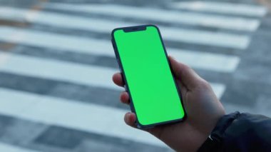 NEW YORK - 19 Aralık 2020: Eller açık havada güneşli cadde üzerinde dikey yeşil arka plan yaya geçidi olan telefonu tutar. Cep telefonu iletişimi dokunmatik ekran dinleme medyası. Yavaş çekim