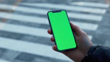 NEW YORK - 19 Aralık 2020: Sokak işçileri, güneşli cadde üzerinde dikey yeşil arka plan yaya geçidi olan telefonu kullanırlar. Cep telefonu iletişimi dokunmatik ekran dinleme medyası. Yavaş çekim