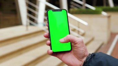NEW YORK - 19 Aralık 2020: Eller, şehrin dışındaki sokakta dikey yeşil ekran arka plan merdivenli telefonu tutar. İletişim, telefon, parmak görüntüleme cihazı. Yavaş çekim