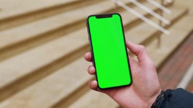 NEW YORK - 19 Aralık 2020: Elle çekilen adam, şehrin dışındaki sokakta dikey yeşil ekran arka plan merdivenli telefonu kullansın. İletişim, telefon, parmak görüntüleme cihazı. Yavaş çekim