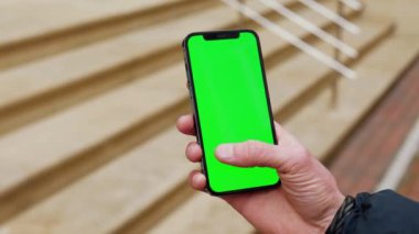 NEW YORK - 19 Aralık 2020: Yavaş çekim yapan adam, şehrin dışındaki sokakta dikey yeşil ekran arka plan merdivenleri olan telefonu kullan. İletişim, telefon, parmak görüntüleme cihazı. Kapat.