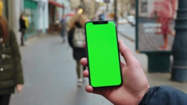 NEW YORK - 19 Aralık 2020: Telefonun arka planında dikey yeşil ekran sokak kenti olan eller açık havada bulanık internet krom kullanıyor. Cep telefonu medya aygıtı. Yavaş çekim