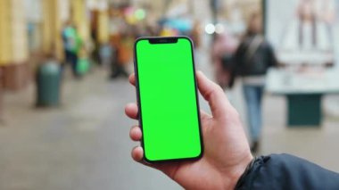 NEW YORK - 19 Aralık 2020: Dikey yeşil ekran arka planda telefon kullanan eller sokak şehrinde yürüyen insanlar açık havada internet krom bulanıklığı yaşıyor. Cep telefonu medya aygıtı. Yavaş çekim