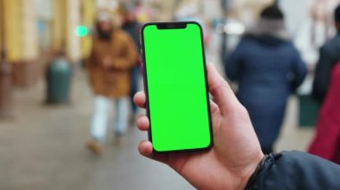 NEW YORK - 19 Aralık 2020: Dikey yeşil ekran arka planda telefon kullanan eller sokak şehrinde yürüyen insanlar açık havada internet krom bulanıklığı yaşıyor. Cep telefonu medya aygıtı. Yavaş çekim