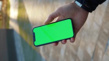 NEW YORK - 19 Aralık 2020: Yakın çekim güneş ışığı için dikey çekim adam açık havada dikey yeşil ekran standı olan telefonu kullanın. Cep telefonu iletişimi dokunmatik ekran dinleme medyası. Yavaş çekim