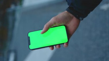 NEW YORK - 19 Aralık 2020: Dikey çekim yapan adam, güneşli caddede yeşil ekran standı olan telefonu kullanıyor. Cep telefonu iletişimi dokunmatik ekran dinleme medyası. Yavaş çekim