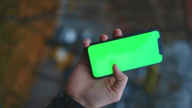 NEW YORK - 19 Aralık 2020: Eski kasabadaki bulanık arka plan görüntüsünde yeşil ekran akıllı telefonu kullanan ve tıklayan dikey çekim adamı eli bulanıklaştı. Dokunmatik ekran cep telefonu. Yavaş çekim