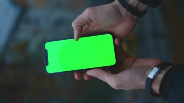 NEW YORK - 19 Aralık 2020: Eski kasabadaki bulanık arka plan görüntüsünde yeşil ekran akıllı telefonu kullanan ve tıklayan dikey çekim adamı eli bulanıklaştı. Dokunmatik ekran cep telefonu. Yavaş çekim