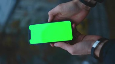 NEW YORK - 19 Aralık 2020: Eski kentteki bulanık arka plan görüntüsünde yeşil ekrandaki akıllı telefonu kullanan ve tıklayan adam bulanıklaştı. Dokunmatik ekran cep telefonu. Dikey çekim. Yavaş çekim