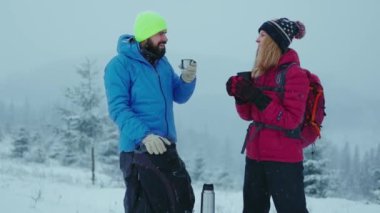 Kış dağları manzarasında sıcak kahve ya da çay içen sevimli bir çift. Seyahat ve macera kavramı. Açık havada yürüyüş, çift ilişkisi. Yavaş çekim
