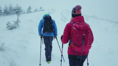 Orman yolundaki kış dağlarında yürüyüş direğiyle kadın ve adamı sırtından vurdu. Sağlıklı soğuk hava yürüyüşçüsü tırmanıyor. Yavaş çekim