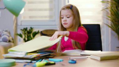 Masanın yanında oturan tatlı kız ödevlerini yapıyor. Evde eğitim ve öğrenim kavramı. Ders kitabı uzak eğitim çocukluğu. Yavaş çekim