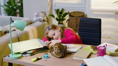 Yazmayı öğrenen bir çocuk ev ödevi yapıyor, masada oturuyor. Kedi etrafta dolanıp kızla oynuyor. Anaokulu çocuğu tek başına ilkokul eğitimi alıyor. Yavaş çekim