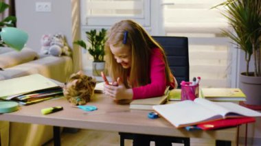 Gülümseyen kız evdeki masada oturup kediyle oynarken iyi eğlenceler. Kedi etrafta dolanıp kızla oynuyor. Anaokulu çocuğu tek başına ilkokul eğitimi alıyor. Kapat.