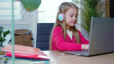 Ciddi çocuk kız koronavirüs salgını sırasında evde kulaklık takıp sohbet ediyor. Uzaktan eğitim kavramı. Online eğitim. Gençlerin uzak interneti. Yavaş çekim