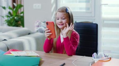 Modern bir evde kalan ve ev ödevlerini telefonda yapan bir kız. Liseli kız portresi karantina altında salgın üzerinde çalışıyor. Masanın yanında oturuyor. Yavaş çekim.