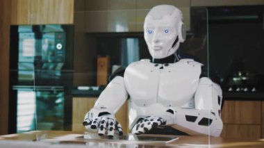 Sibernetik otomatik beyaz robot işçisi klavyesini daktilo ederek dijital bilgilerin çalıştığı ve dairedeki verileri aradığı şeffaf holografik ekrana bakıyor..