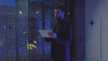 Tablet bilgisayarda çalışan bir iş adamı mavi ışığı olan bir odada şeffaf ekran kullanır. İşçi, çek, ofis, pazarlama, dokunmatik ekran. Yavaş çekim