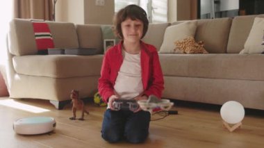 Küçük sevimli çocuk oyuncak kuadkopter uçuruyor uzaktan kumandalı joystick kullanarak eğleniyor. Mutlu çocuk etkileşim teknolojisi evde modern oyuncaklarla oynuyor..