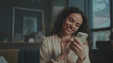 Mutlu bir kadın akıllı telefonuyla iletişim kurar, mutluluk ve bağlılık duygularını kapalı bir ortamda gösterir..