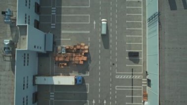 Hareket halindeki kamyonlarla dolu hava yükleme iskelesi, rıhtımlara park etmiş çok sayıda römork, palet yığınları ve forkliftler, işaretli şeritler ve yön okları.,