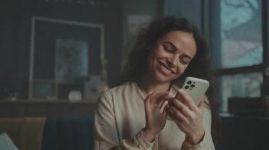 Gülümseyen beyaz kadın telefon ekranına dokunuyor, yumuşak doğal ışık, çerçevelenmiş sanat arkaplanı, sohbet baloncuklarıyla duygusal ilişki,