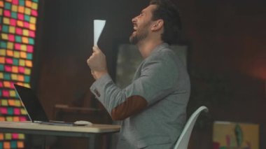 Beyaz adam dizüstü bilgisayara tezahürat ve yumruk pompasıyla tepki veriyor sonra da strese girip sonuç için dua ediyor, modern ofis.