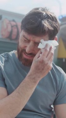 Kanayan erkek, ambülansın yanındaki burnu siler, sersemlemiş ifade ve çürük yüz, tozlu giysilerin üzerindeki güneş ışığı.,