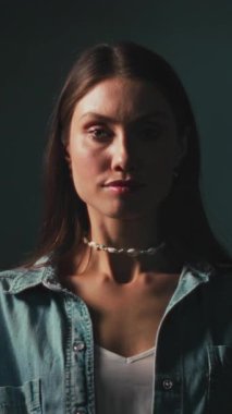 Kafkasyalı kadın loş bir stüdyoda, düşünceli yan profil, kot gömlek, kabuk tutucu, sinema gölgeleri...