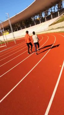 Stadyum aralığı siyah antrenör beyaz koşucu kırmızı şeritler boyunca tempo tutuyor, dinamik koçluk ipuçları ve ölçülü tur ipuçları.