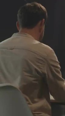 Masadaki beyaz adam belgeleri ve telefon tarama raporlarını inceleyerek notlar alıyor. Konsantrasyon için yumuşak pencere ışığı.