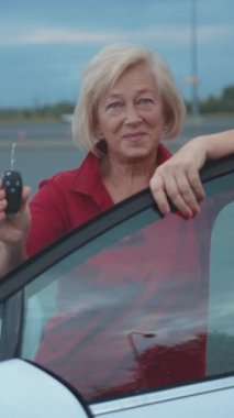 Son sınıf öğrencisi kadın arabanın anahtarını açık kapının yanında tutuyor. Dostane bir gülümsemesi var. Araca yaslanıyor, akşam gökyüzü arka planında, kendinden emin.